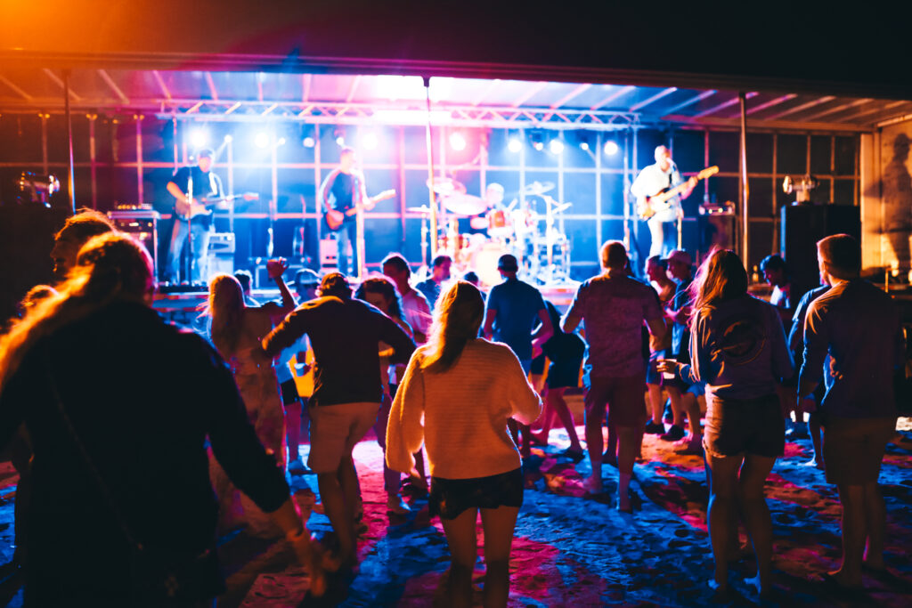 A group of people stands on a stage at night, illuminated by stage lights, with a dark sky in the background
