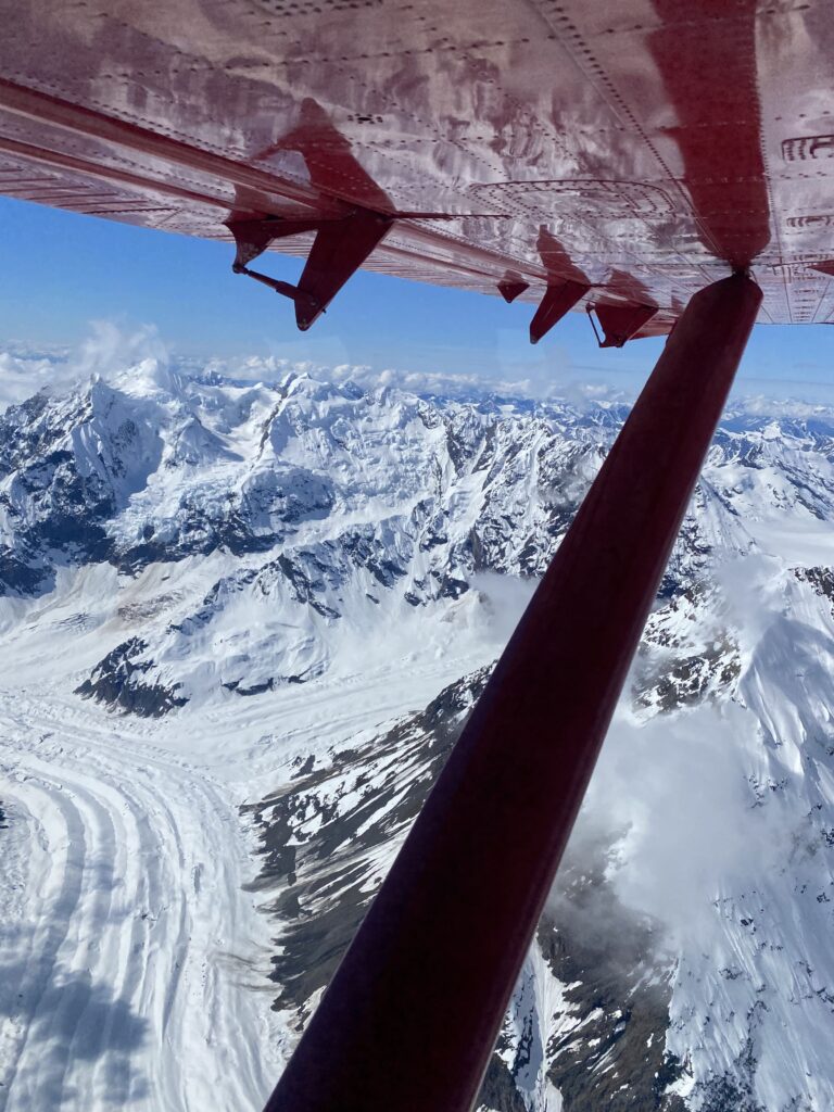 View from an airplane wing capturing a glacier's expansive ice field and unique formations beneath