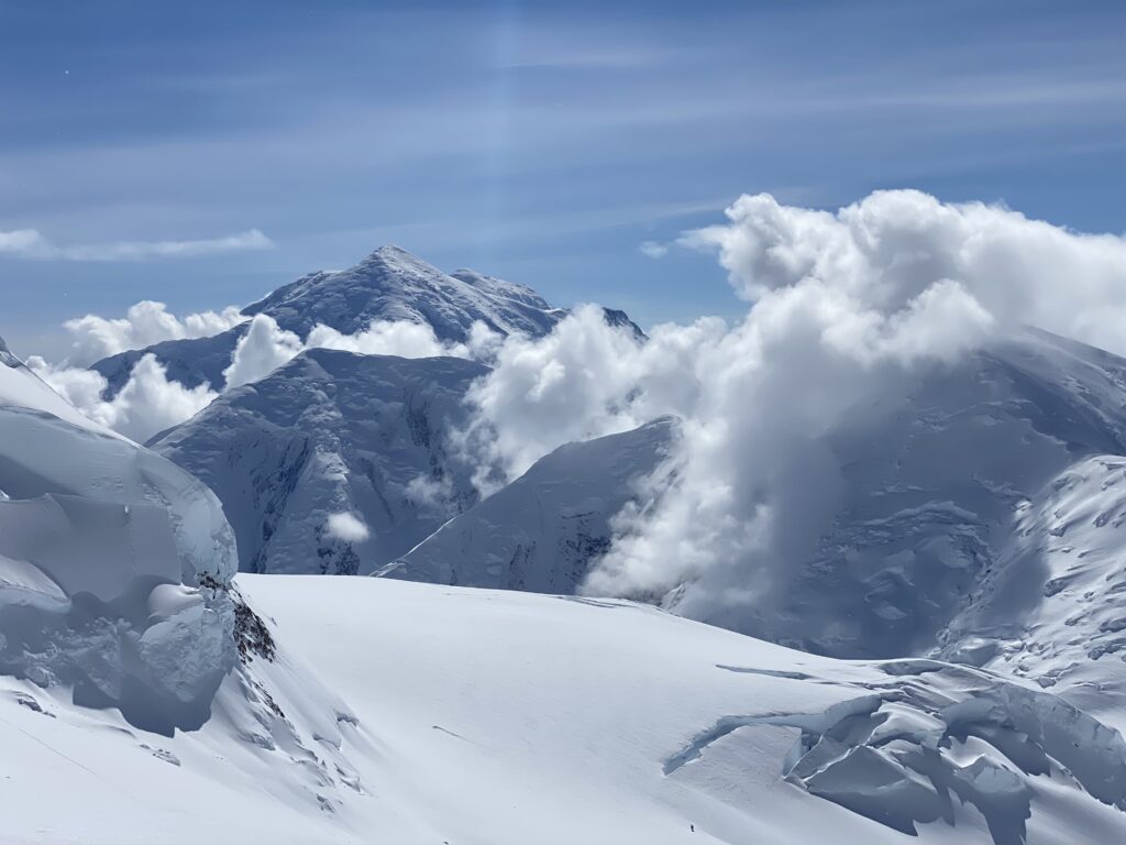 Snow-covered mountain summit offering a breathtaking view of surrounding peaks and valleys under a bright blue sky